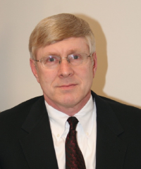 Headshot of Kirk Michealson in a black suit and red tie infront of a cream colored background